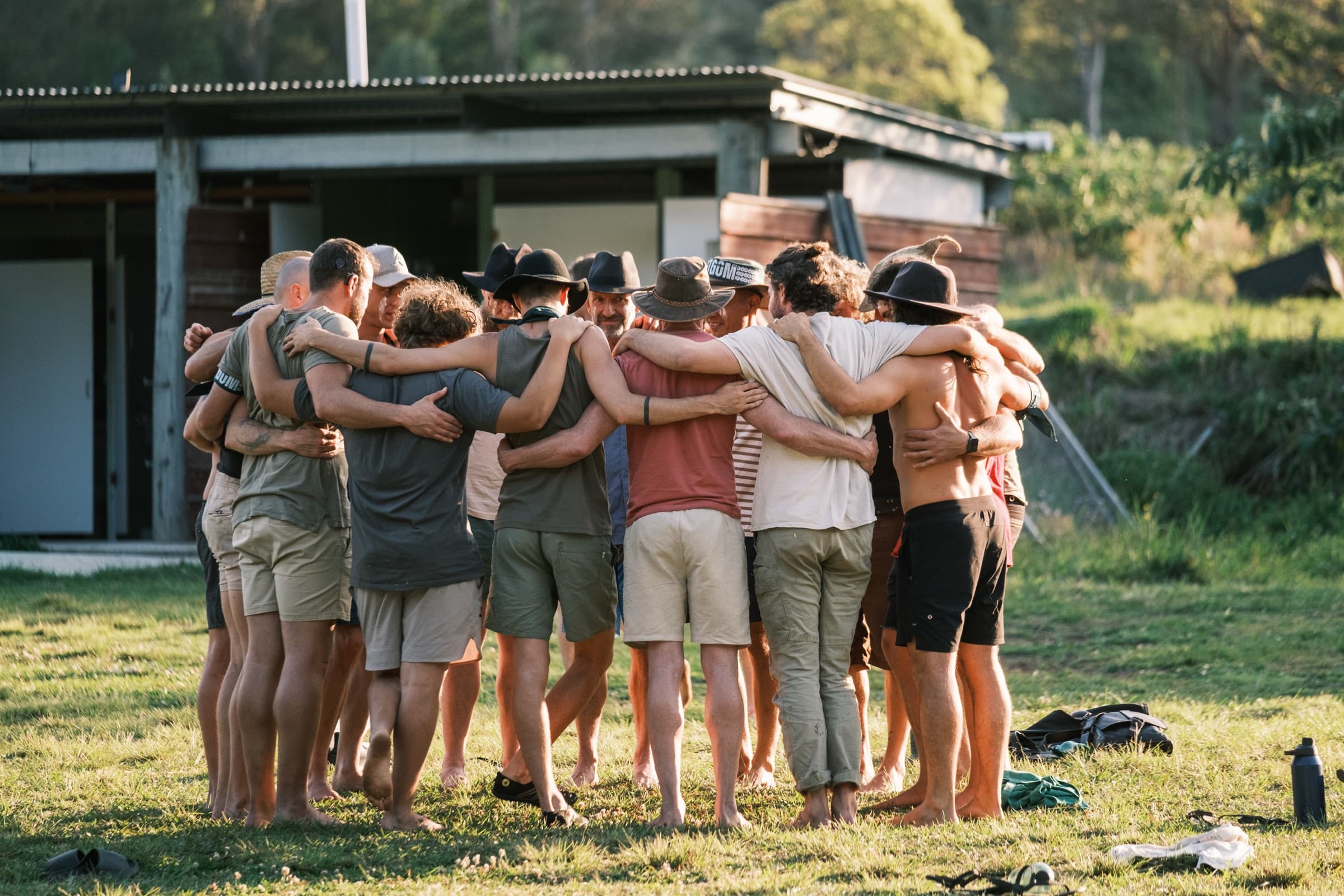 A circle of men, arms around one another, at sunset